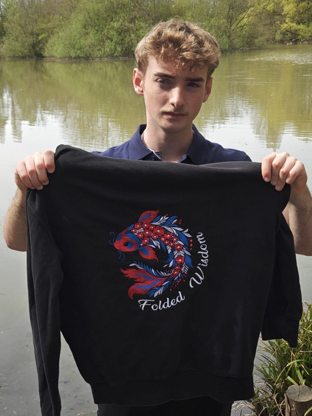 Holding up a black sweatshirt with the koi embroidery by the lake