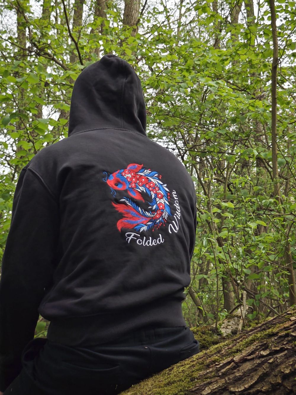 Back of a black hoodie with the koi embroidery, among trees
